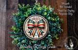 A wreath made of green leaves and a circular metal plaque with an American flag design, including a ribbon and the text "God Bless America 250th".