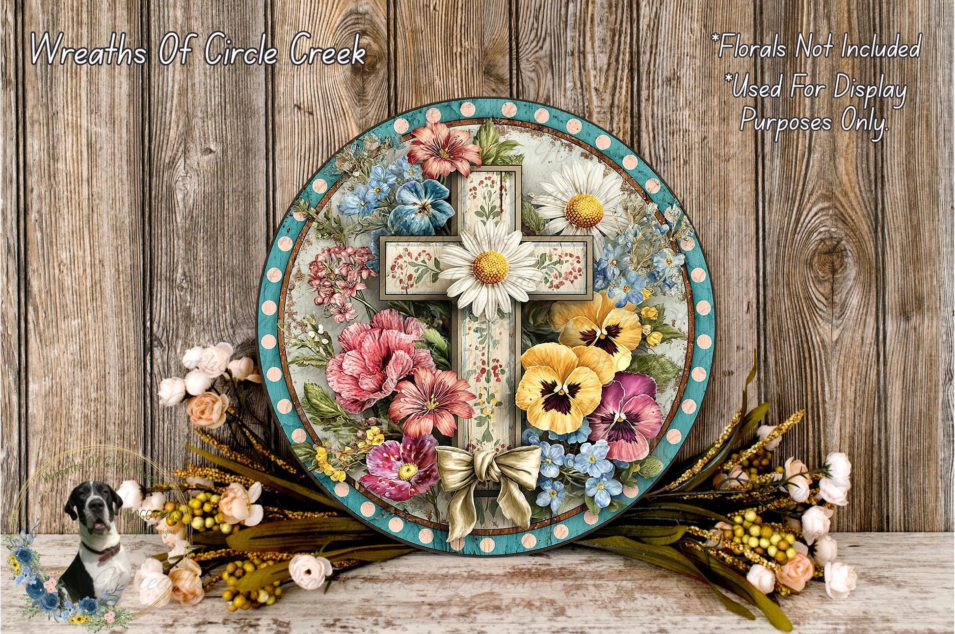 A decorative wreath with a cross and various colorful flowers, including daisies, pansies, and other blooms, is displayed on a wooden surface.