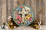 A decorative wreath with a cross and various colorful flowers, including daisies, pansies, and other blooms, is displayed on a wooden surface.