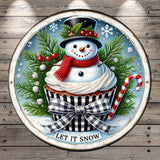 A snowman wearing a red scarf and hat sits atop a cupcake, surrounded by pine branches, berries, and a candy cane, with the text "LET IT SNOW" displayed below.