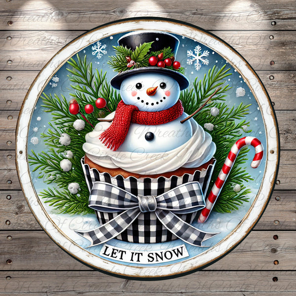 A snowman wearing a red scarf and hat sits atop a cupcake, surrounded by pine branches, berries, and a candy cane, with the text "LET IT SNOW" displayed below.