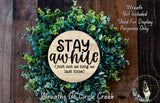 a wreath made of green leaves and a wooden sign with the text "STAY AWHILE" in the center.