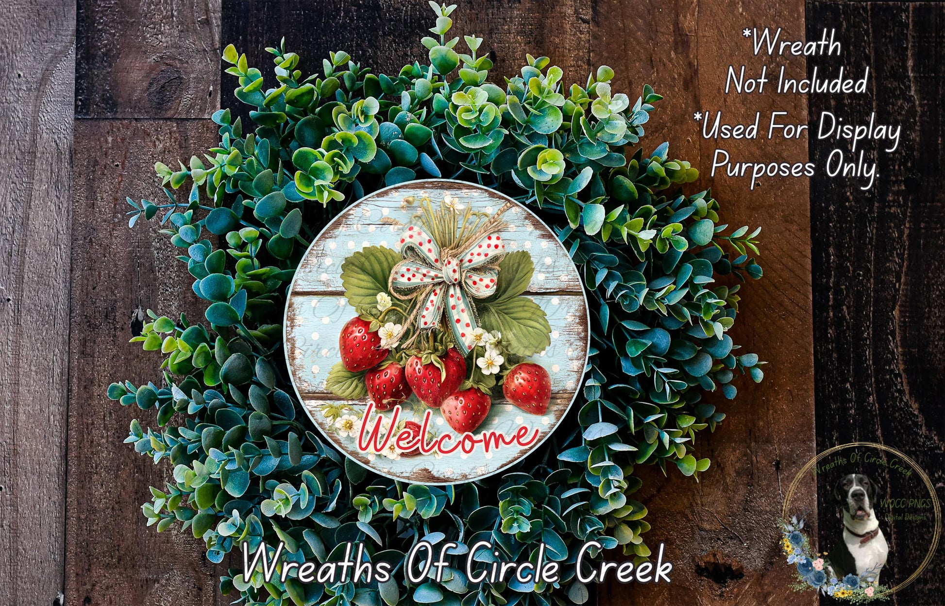 a wreath made of various green plants and red berries, with the word "Welcome" written on it. The wreath is displayed on a wooden surface, and there is a small dog in the bottom right corner of the image.