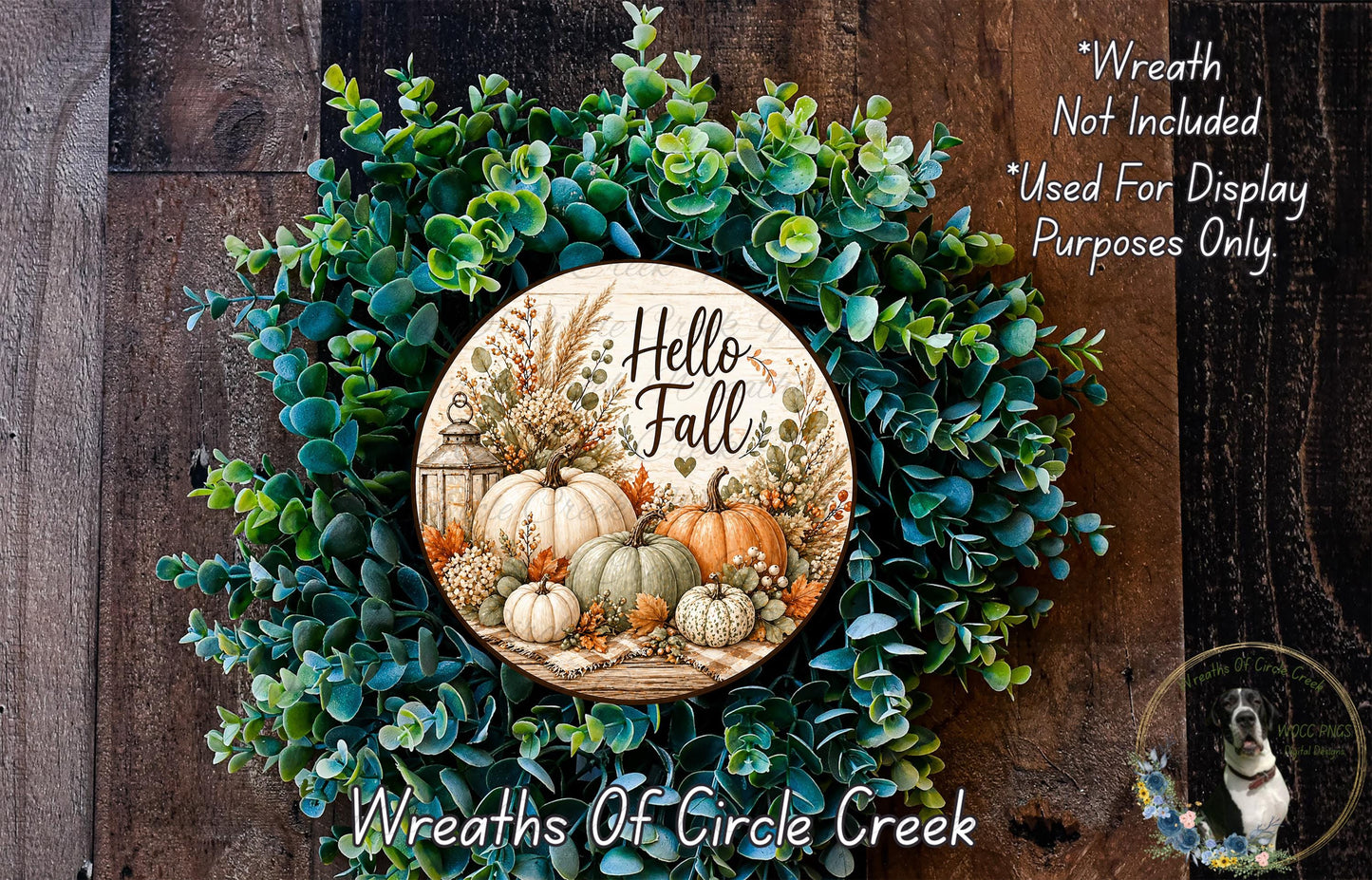 a wreath made of various fall-themed elements, including pumpkins, leaves, and pine cones, with the phrase "Hello Fall" written on it. The wreath is displayed on a wooden surface, and there is a small dog in the bottom right corner of the image.