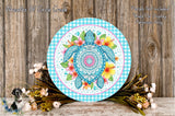 a decorative round plate with a blue and white checkered border, depicting a colorful turtle surrounded by flowers and leaves. The plate is placed on a wooden surface, with a bouquet of flowers and leaves arranged around it.