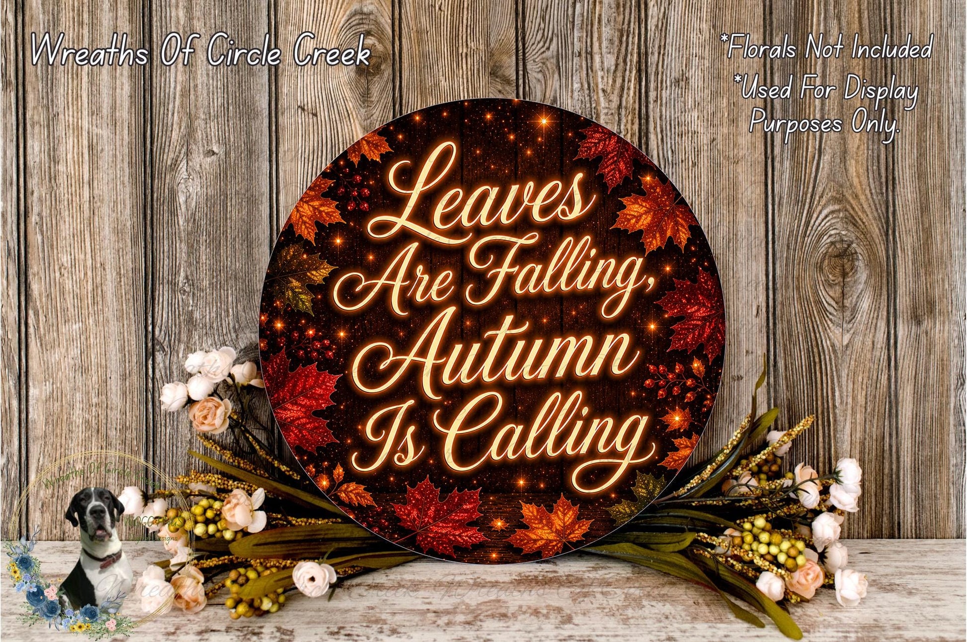 a circular sign with the text "Leaves Are Falling, Autumn Is Calling" surrounded by autumn leaves and flowers, placed on a wooden surface.