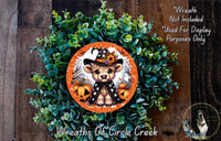 A wreath made of green foliage and orange and white accents, featuring a cartoon character wearing a witch's hat and holding a pumpkin.