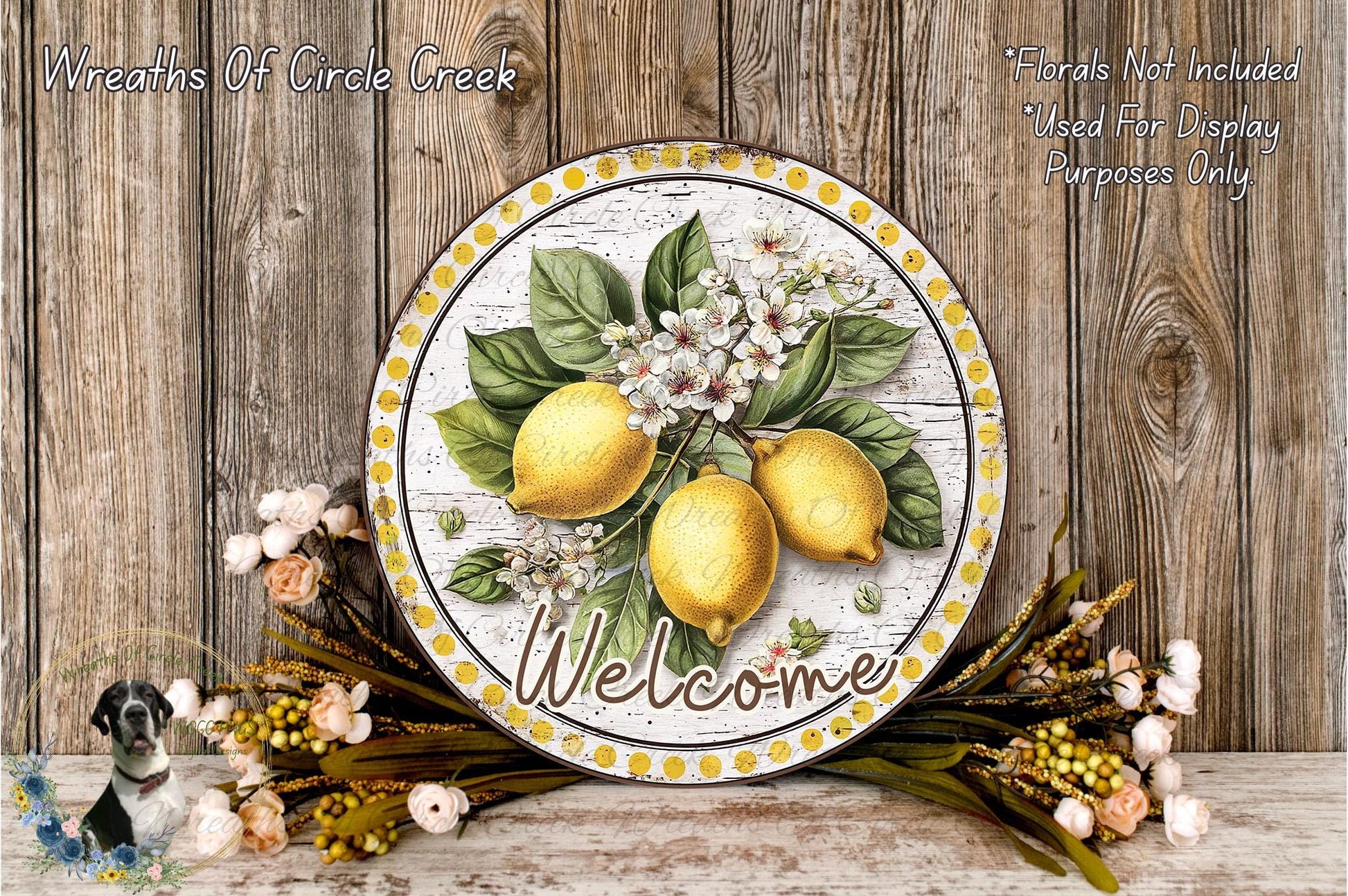 a decorative sign with a lemon and flower design, surrounded by a wreath of flowers and greenery, placed on a wooden surface.