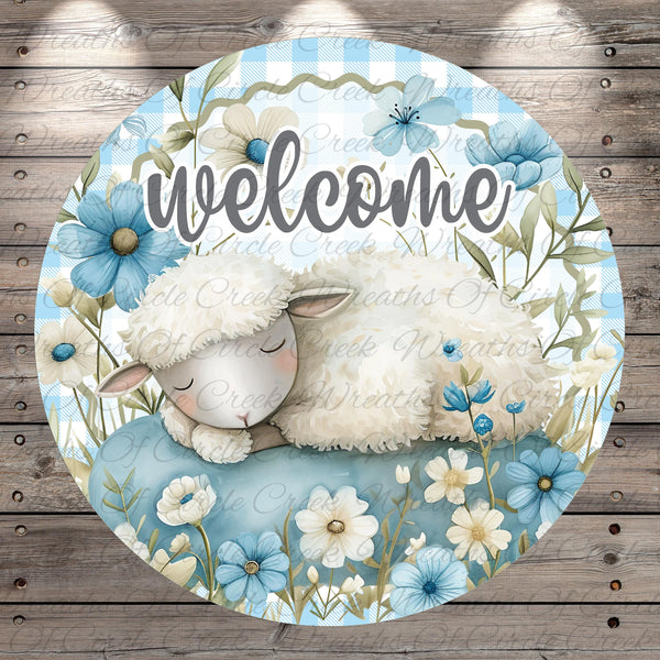 A round, decorative sign featuring a sleeping lamb surrounded by blue flowers and greenery.