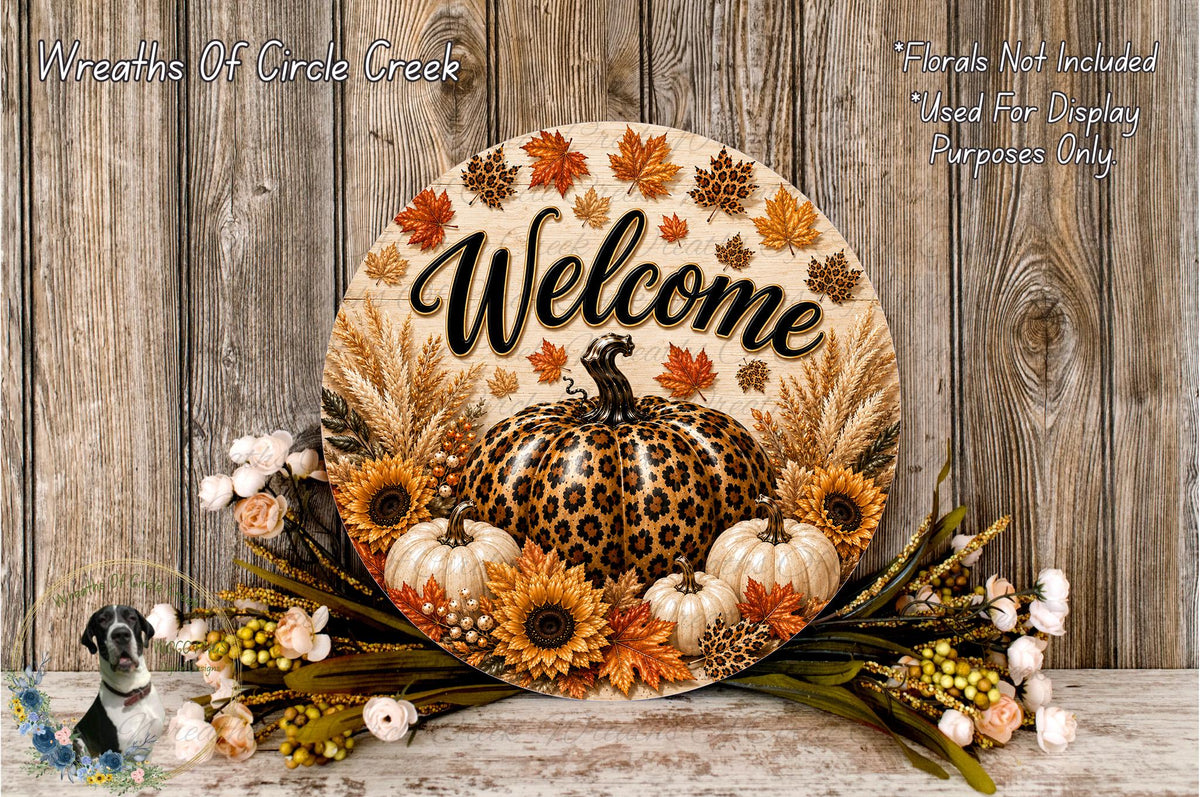 a decorative welcome sign with a leopard print pumpkin and autumn foliage, surrounded by flowers and placed on a wooden surface.