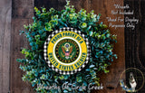 A wreath made of green leaves and a yellow and black emblem, representing the United States Army, is displayed against a wooden background.