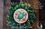 A wreath made of various green plants and flowers, with a large circular design featuring a turtle surrounded by colorful flowers.