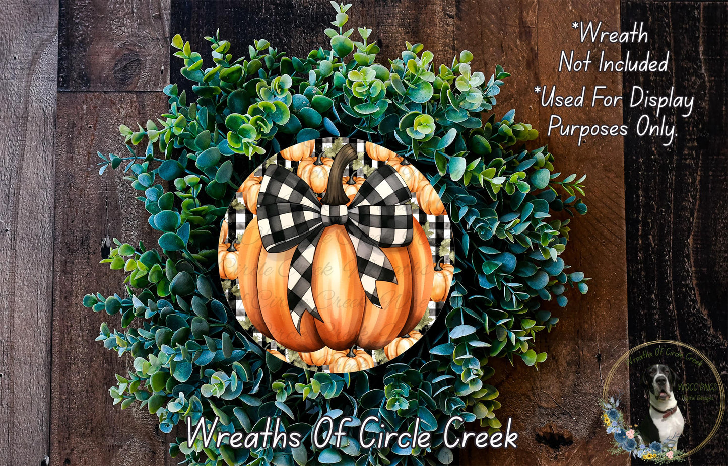 a wreath made of various green plants and a large orange pumpkin with a black and white checkered bow, hanging on a wooden wall.