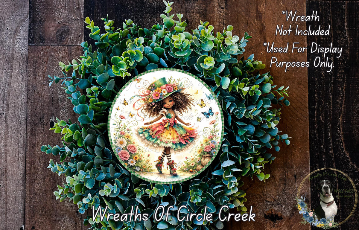 a wreath with a central image of a fairy wearing a colorful dress and hat, surrounded by a lush green wreath. The wreath is displayed on a wooden surface, and there is a small dog in the bottom right corner of the image.