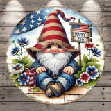 A gnome wearing a red, white, and blue striped hat sits on a wooden bench surrounded by flowers and a sign that reads "Happy 250".