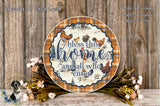 a decorative plate with a plaid pattern and a message that says "bless this home and all who enter." The plate is surrounded by a floral arrangement and placed on a wooden surface.