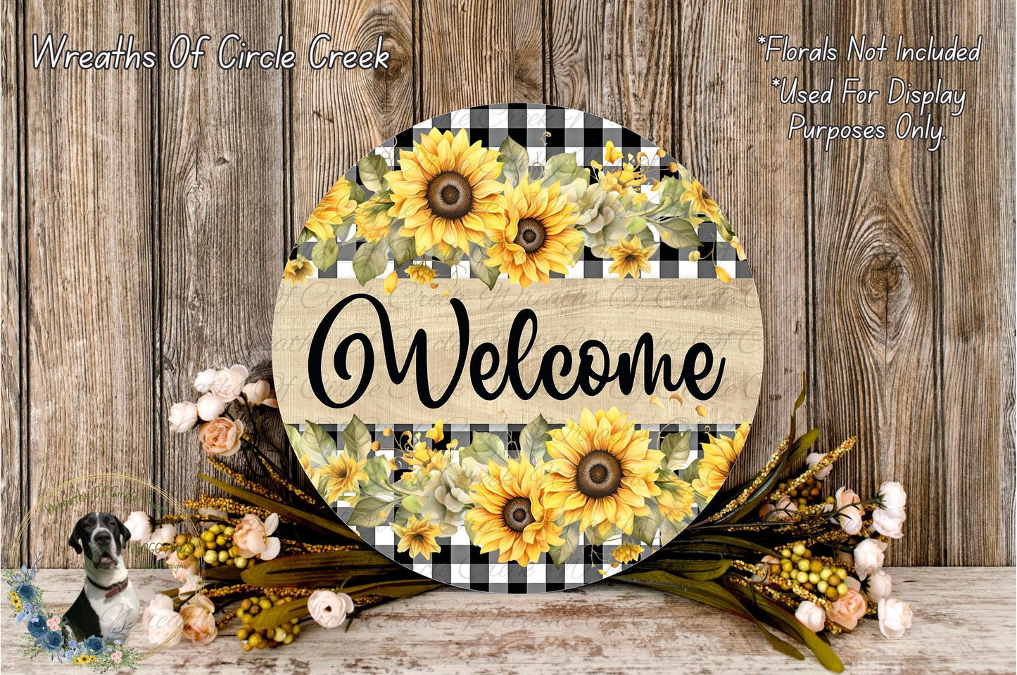 a circular wooden sign with a floral design, surrounded by a wreath of flowers and greenery, placed on a wooden surface.