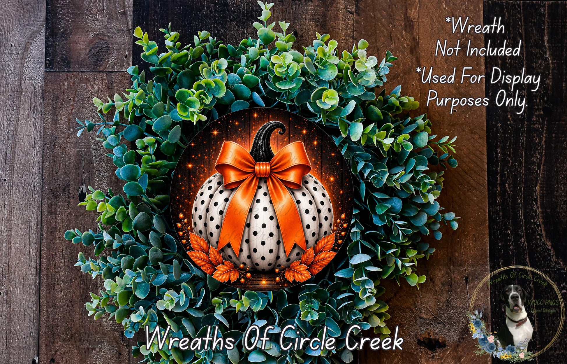 a wreath with a white pumpkin and orange polka dots, surrounded by green foliage. The wreath is displayed on a wooden surface, and there is a small dog in the bottom right corner of the image.