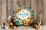 a decorative welcome sign with a floral design, surrounded by pumpkins, sunflowers, and other fall-themed elements. The sign is placed on a wooden surface, with a wreath of flowers and pumpkins nearby.