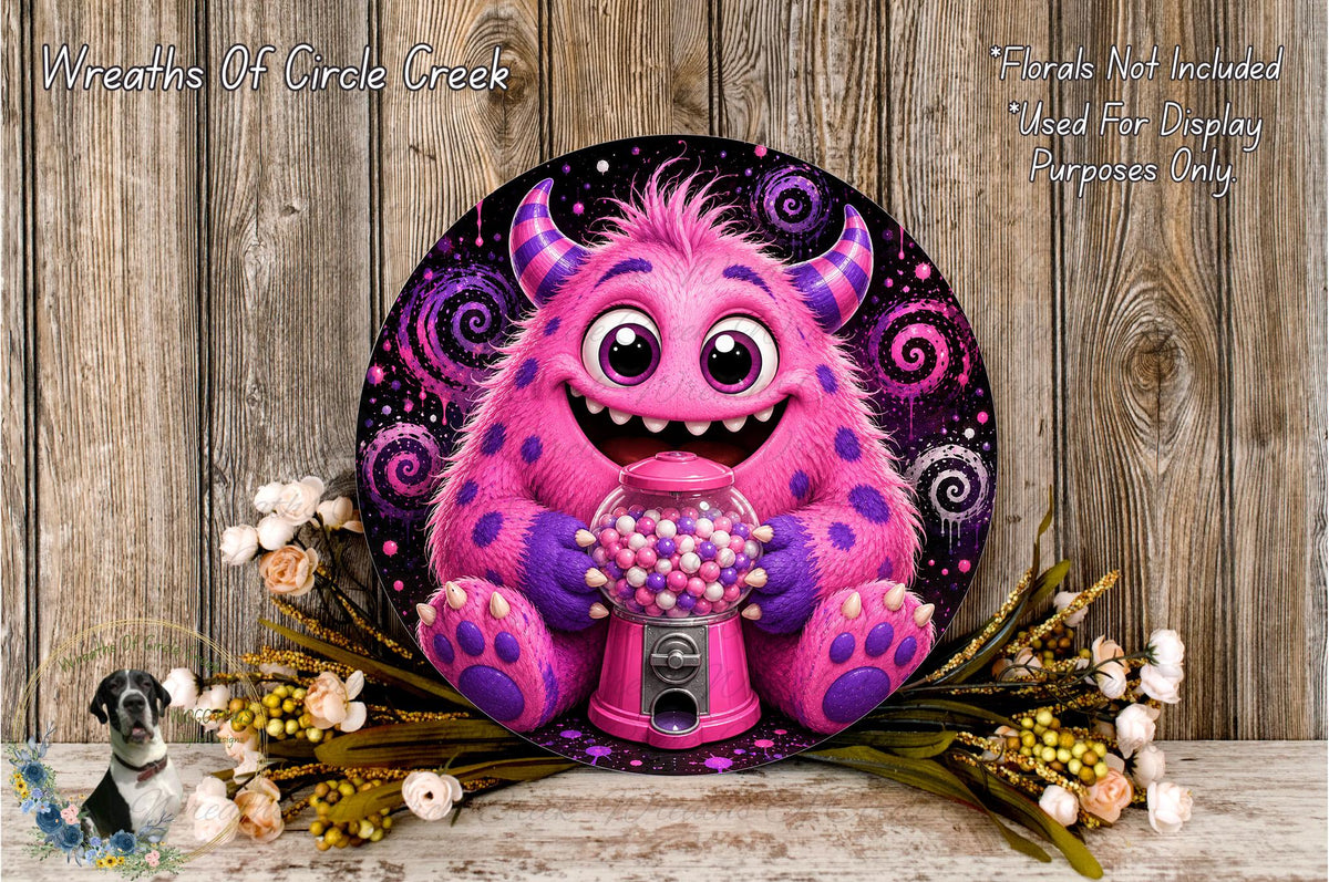 A whimsical, cartoonish monster with horns and a big smile is sitting in front of a pink gumball machine, surrounded by flowers and a wooden background.