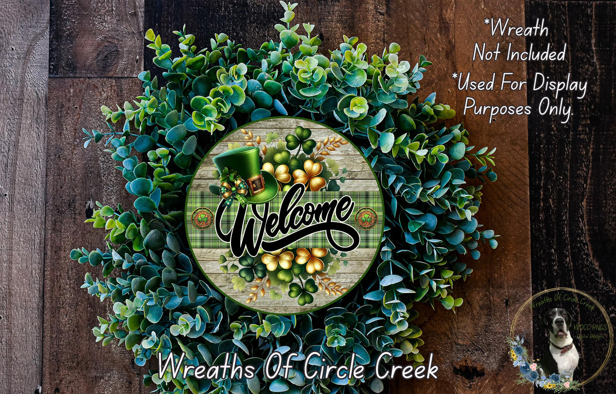 a wreath with a welcome sign in the center, surrounded by various green plants and flowers. The wreath is displayed on a wooden surface, and there is a small dog in the bottom right corner of the image.