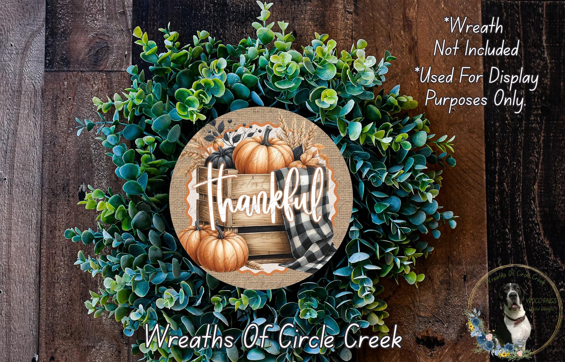 a wreath made of green leaves and pumpkins, with the word "Thankful" written on it. The wreath is displayed on a wooden surface, and there is a small dog in the bottom right corner of the image.