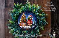 A wreath featuring a Christmas tree with a cartoon alligator wearing a red sweater and a Santa hat, surrounded by greenery.