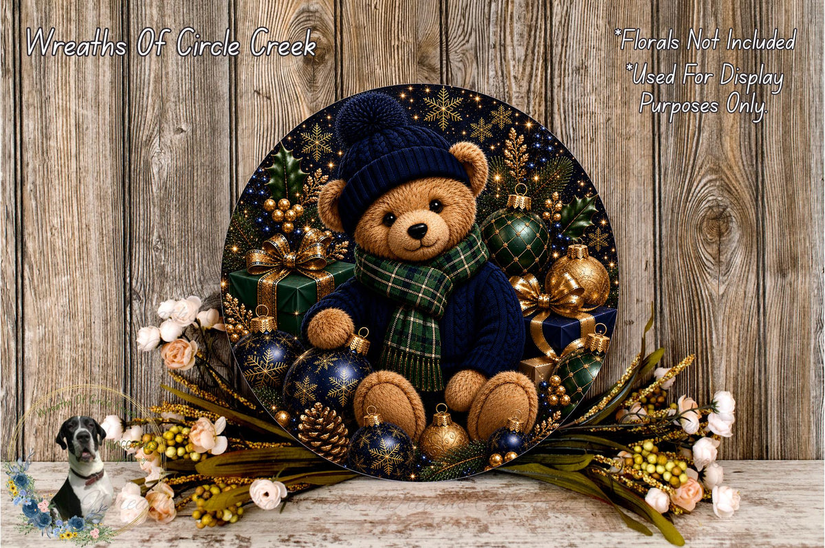 A decorative wreath featuring a teddy bear wearing a blue hat and scarf, surrounded by Christmas ornaments and flowers, placed on a wooden surface.