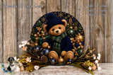 A decorative wreath featuring a teddy bear wearing a blue hat and scarf, surrounded by Christmas ornaments and flowers, placed on a wooden surface.
