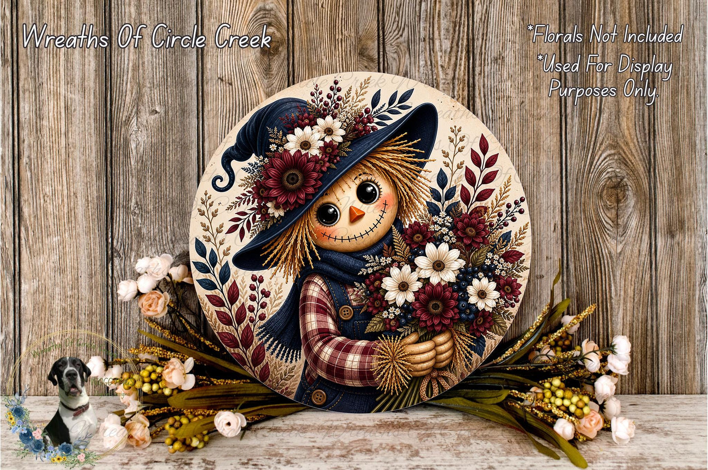 A decorative round wreath with a scarecrow figure holding a bouquet of flowers, placed on a wooden surface.