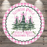 A circular sign with a pink and white checkered border, featuring three Christmas trees with pink bows. The sign has the text "NORTH P Pole" and "FARM FRESH CHRISTMAS TREES" written on it.