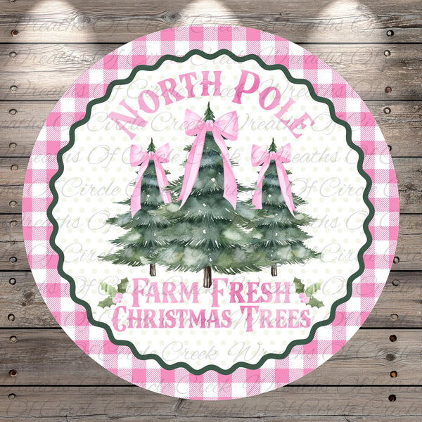 A circular sign with a pink and white checkered border, featuring three Christmas trees with pink bows. The sign has the text "NORTH P Pole" and "FARM FRESH CHRISTMAS TREES" written on it.
