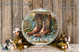 a round wooden sign with a pair of brown cowboy boots on it, surrounded by flowers and greenery. The sign has the text "Kick off your boots" written on it.