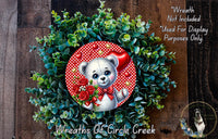 A wreath made of green leaves and red flowers, with a cute white teddy bear wearing a red bow tie and holding a bouquet of red roses.