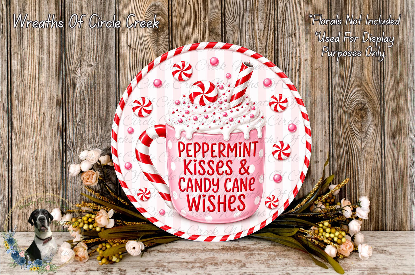 A decorative wreath with a peppermint mug and candy cane, surrounded by flowers and greenery, against a wooden background.