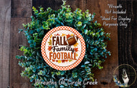 a wreath made of green leaves and a football, with the text "FALL Family Football" displayed on it. The wreath is placed on a wooden surface, and there is a small dog in the bottom right corner of the image.