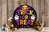 a Halloween-themed sign with the text "TRICK OR TREAT" surrounded by ghostly figures and a full moon. The sign is placed on a wooden surface, with a floral arrangement and some flowers nearby.