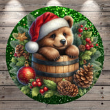 A brown bear wearing a Santa hat is sitting in a wooden barrel surrounded by Christmas decorations, including pine cones, berries, and a star.