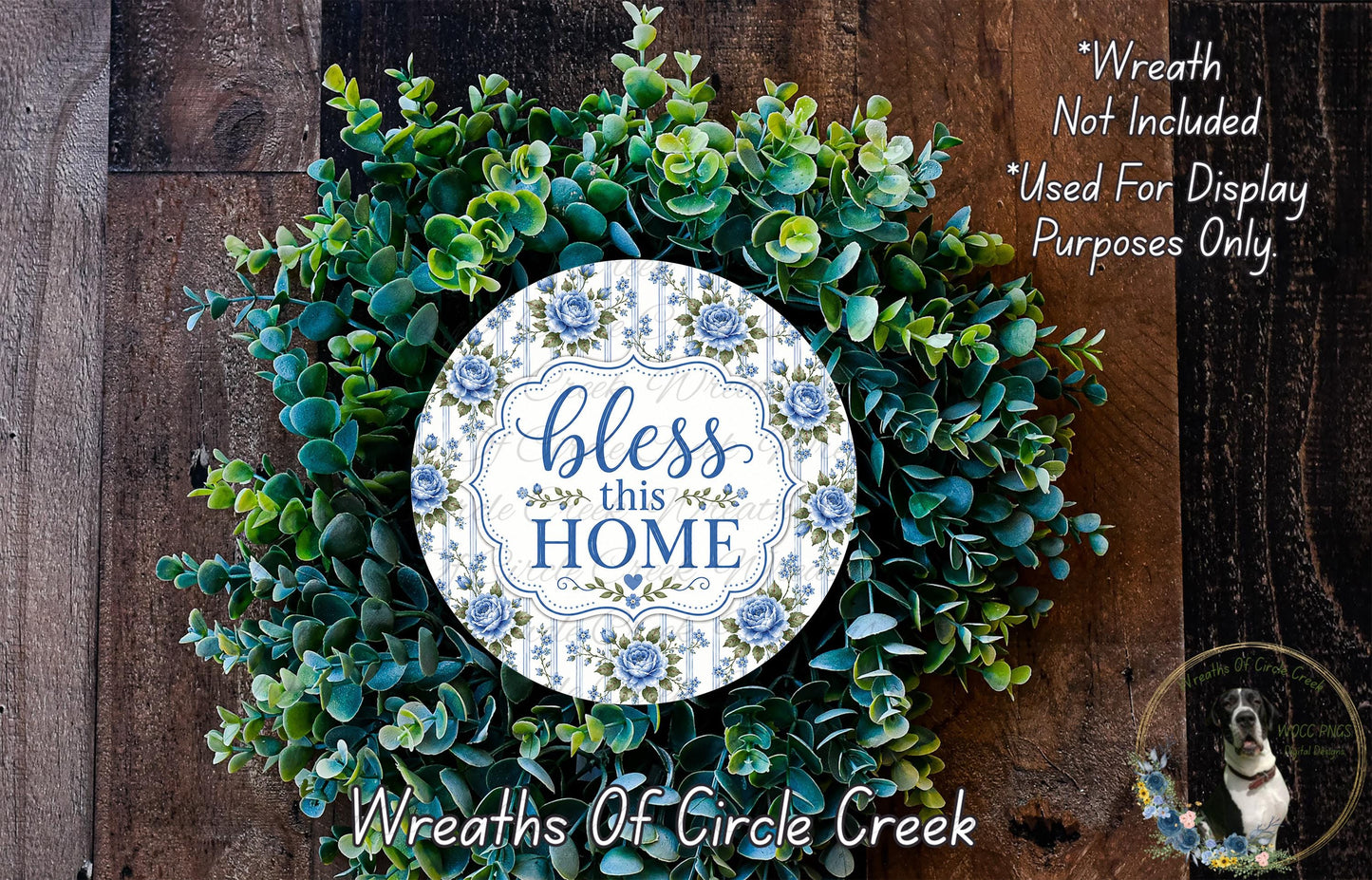 A wreath made of various green plants and flowers, with a white circular sign that says "bless this home" in blue and green lettering.