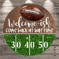 A welcome sign with a football and the text "Welcome-ish, come back at half-time" on a wooden background.