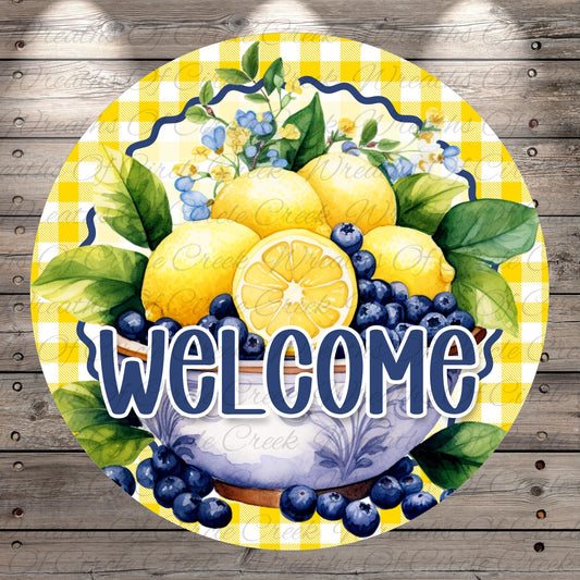 A round sign with a bowl of fruit, including lemons, blueberries, and green leaves, surrounded by a yellow and white checkered pattern. The sign has the text "WELCOME" written on it.