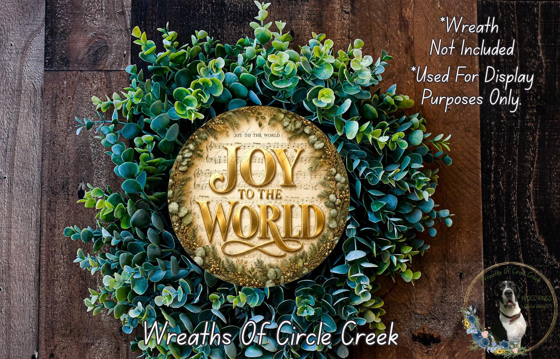 a wreath with the text "Joy to the World" on it, surrounded by green leaves and flowers. The wreath is displayed on a wooden surface, and there is a small dog in the bottom right corner of the image.