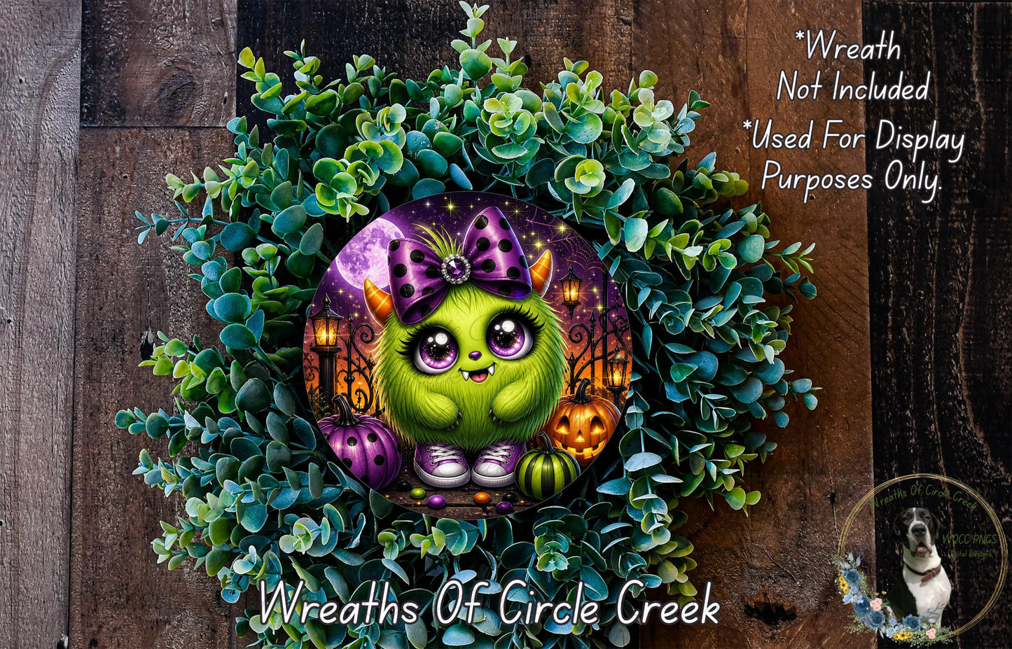 A whimsical wreath featuring a green monster with purple horns and a purple bow, surrounded by a lush green plant and Halloween-themed decorations.