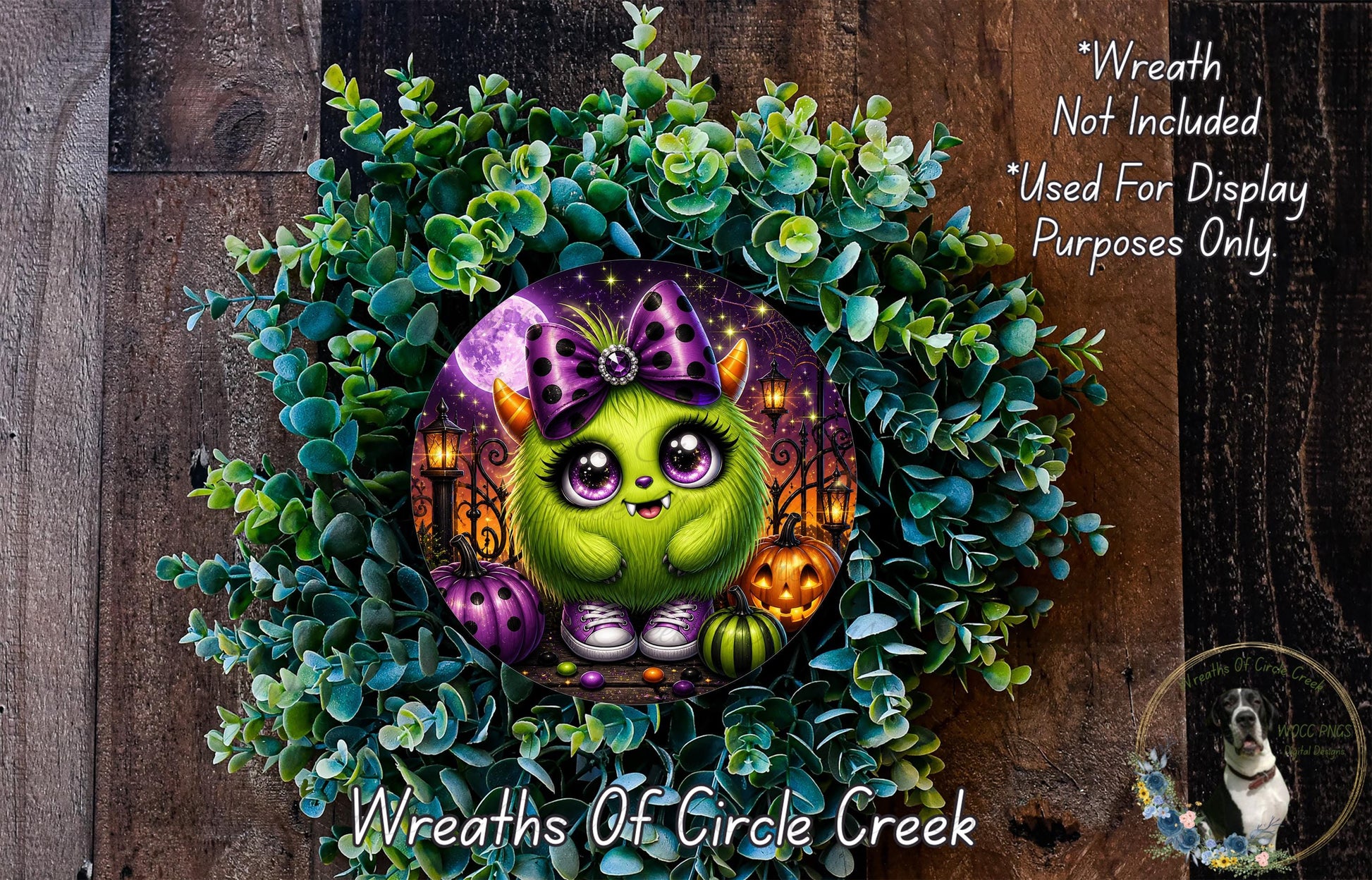 A whimsical wreath featuring a green monster with purple horns and a purple bow, surrounded by a lush green plant and Halloween-themed decorations.