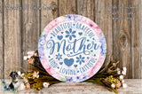 a decorative sign with the text "Beautiful Graceful Mother" surrounded by flowers and greenery. The sign is placed on a wooden surface, and there is a small dog in the background.