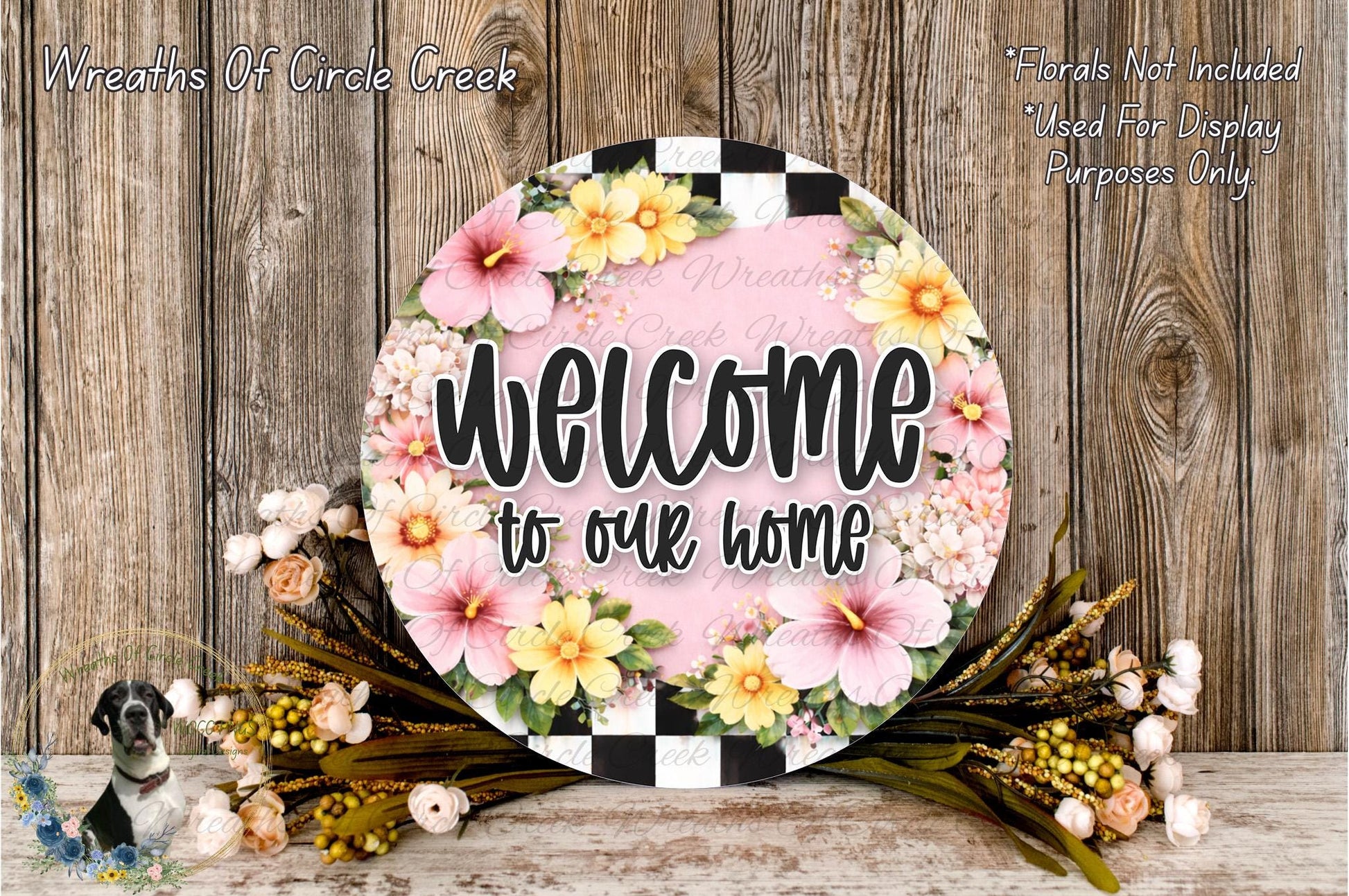 a round sign with a floral design, surrounded by a wreath of flowers and greenery, placed on a wooden surface.