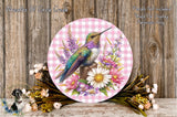 A round decorative plate featuring a colorful hummingbird surrounded by flowers and foliage, placed on a wooden surface.