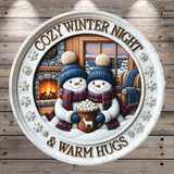 A cozy winter night scene featuring two snowmen sitting by a fireplace, with a mug of hot chocolate between them. The text "COZY WINTER NIGHT & WARM HUGS" is displayed around the snowmen, creating a warm and inviting atmosphere.