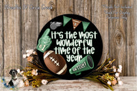 A black circular sign with a football, a cheerleader, and a football trophy, surrounded by flowers and greenery, with the text "It's the most wonderful time of the year" displayed on it.