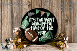 A black circular sign with a football, a cheerleader, and a football trophy, surrounded by flowers and greenery, with the text "It's the most wonderful time of the year" displayed on it.
